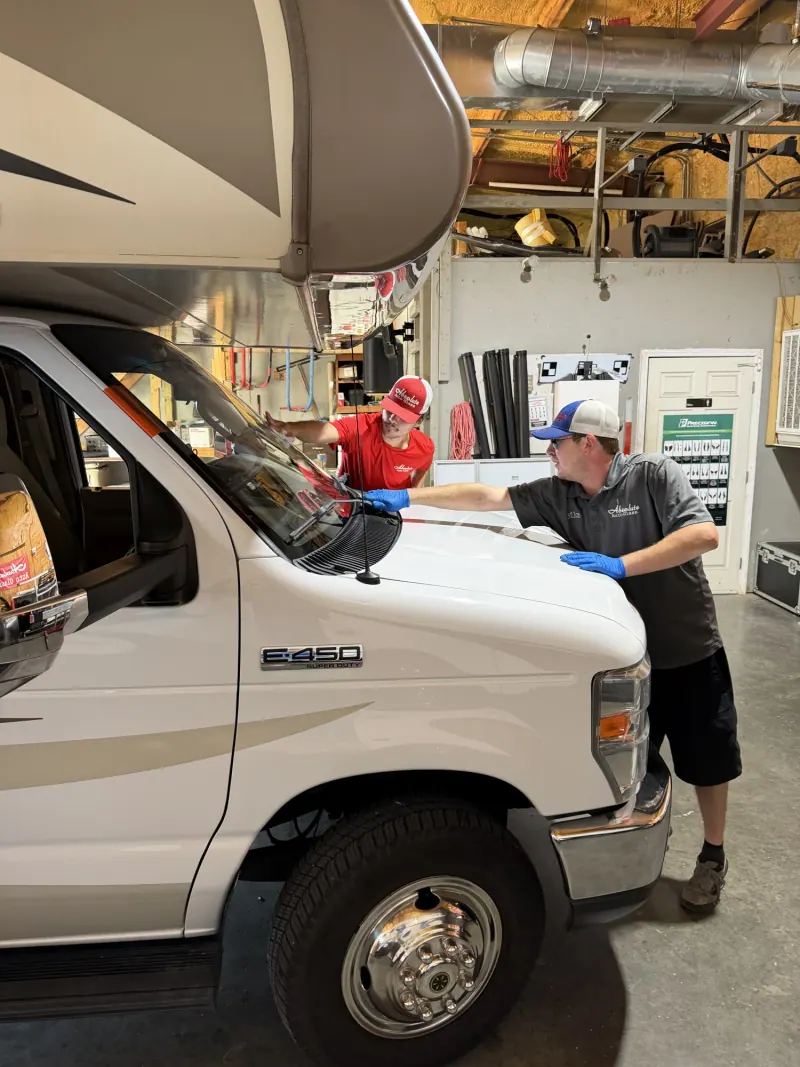 Two Absolute Auto Glass technicians working at a Class C motorhome windshield